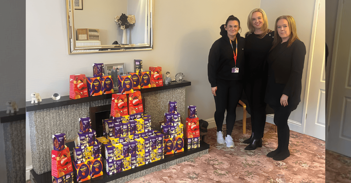 Staff from Varty's Funeral Directors in Wigan stand next to a large display of Cadbury Easter eggs stacked on a fireplace hearth.